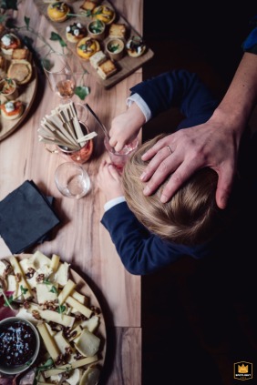   At Art Restaurant in Lyon, Rhône, France, a young child’s blond head is visible from above as their small hands eagerly reach for food at the freshly set buffet table.